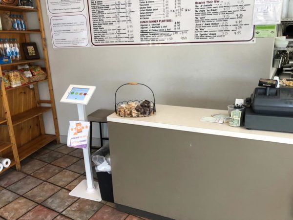 A tidy counter at a casual eatery displaying a Mobile Review Generation kiosk, a menu board in the background, and a basket of cookies inviting customers to add a sweet treat to their order.
