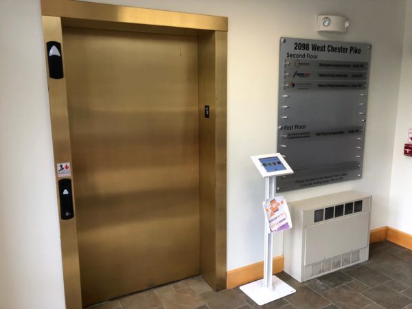 An elevator entrance next to a building directory sign and an information kiosk in a modern indoor setting.